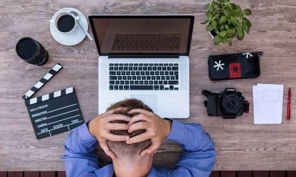 办公室场景中一位设计师在电脑前对照蜜桃网站界面截图记录改版建议，屏幕呈现紫粉配色